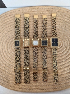 Detail of leopard print mesh strap and gold quartz watch dials on a woven mat