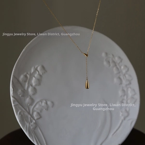 Detailed macro view of 18K gold plated Y-necklace with smooth teardrop pendants on ceramic