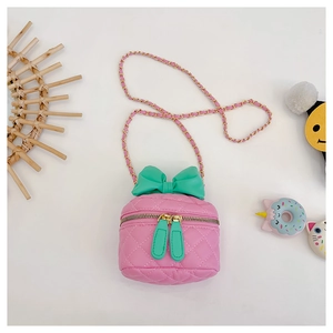 Detail of pink quilted girl's handbag featuring a large green bow and gold chain strap