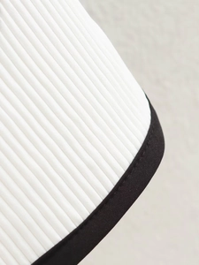 Detail of white pleated fabric with black contrast binding and sharp stitching on the garment