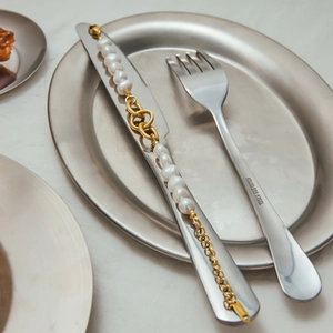 Macro shot of 18k gold plated pearl necklace wrapped around stainless steel cutlery