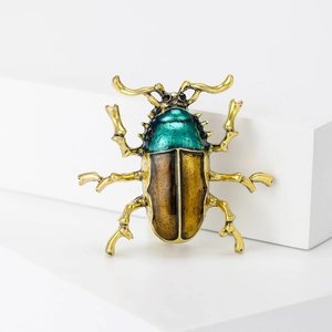 Golden beetle enamel brooch with teal and brown wing details on a white platform