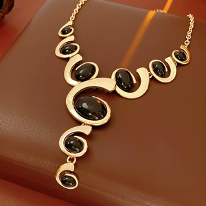 Close-up of golden geometric necklace with black oval gemstones on brown leather