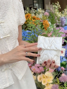 Quilted heart pouch in off-white with snap button held in a colorful floral setting