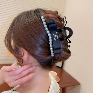 Detail view of black bow hair claw with elegant pearls and golden metal logo accent