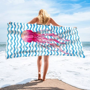 Microfiber beach towel with pink jellyfish and blue wave stripes on a sunny shore