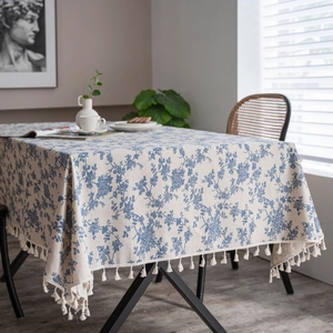 Detail of linen table cloth with blue floral patterns and decorative tassels on the edges