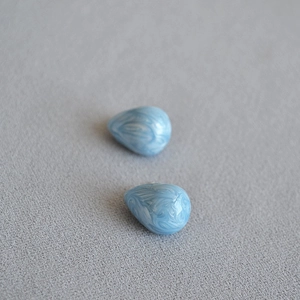 Macro detail of light blue pear-shaped earrings with marble texture and gold plating