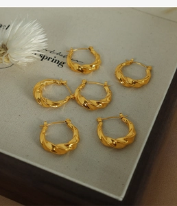 Détail macro de trois paires de boucles d'oreilles créoles dorées torsadées sur tissu