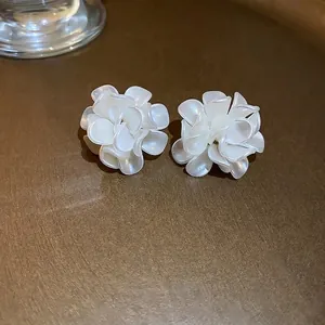 Détail de boucles d'oreilles camélia avec pétales blanc crème sur fond texturé de luxe