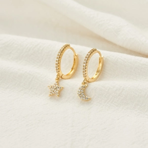 Detail of gold moon and star earrings with pavé cubic zirconia on textured fabric