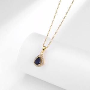 Macro shot of gold necklace featuring teardrop blue stone surrounded by tiny white diamonds