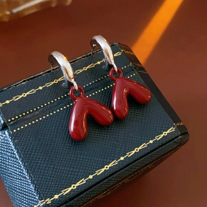 Close-up of red heart pendant earrings with silver hoops on a vintage jewelry box