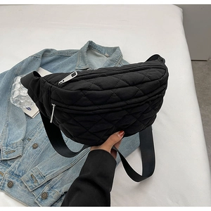 Detailed view of a black quilted crossbody waist bag with wide strap held by a model