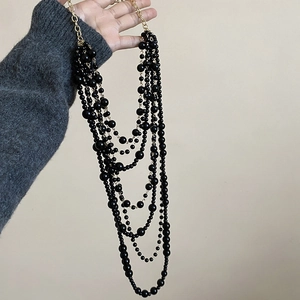 Detail of layered black acrylic beads and gold chain necklace shown on a hand