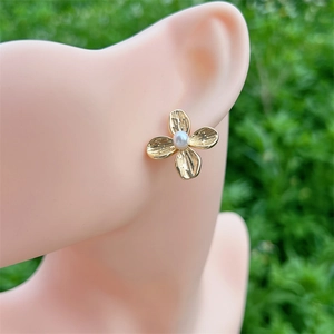 Elegant gold flower stud earrings with white pearl center on model with nature background