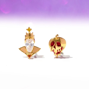 Macro view of asymmetrical gold earrings with crown and red poison apple motifs