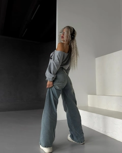 Détail d'un jean évasé bleu délavé taille haute avec sweat gris à épaules dénudées style rue