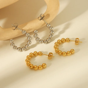 Detail view of gold and silver beaded C-shaped stud earrings on a minimalist stone