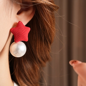 Close-up of red fabric star and white pearl drop earring worn on model's ear