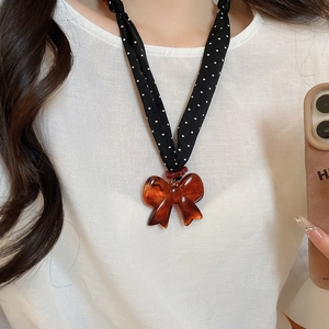 Close-up of retro necklace featuring a black polka dot fabric band and amber bow pendant