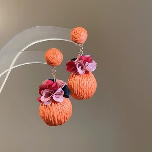 Close-up of orange raffia woven double ball earrings with colorful fabric flower accents