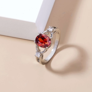 Close-up of a silver ring with an oval red gemstone and side cubic zirconia accents