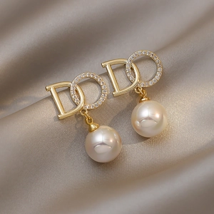 Macro view of gold pearl earrings with a sparkling zircon ring on champagne silk