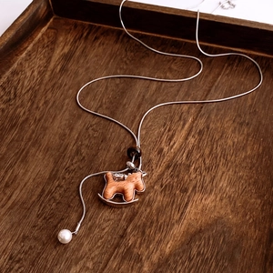 Detail of a rocking horse pendant on a long silver necklace with a white pearl accent