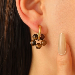 Close-up of golden hoop earrings featuring a tiger eye stone flower pendant on a model