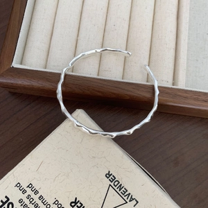 Detail of S925 sterling silver open cuff bracelet with hammered wavy texture on wood