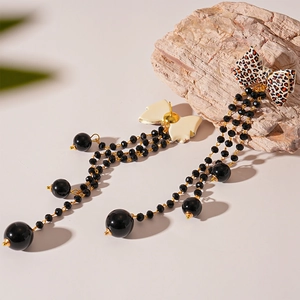 Detail of leopard print bow earrings with black beaded tassels on natural stone