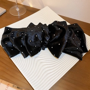 Detail shot of a black fabric bow hair claw clip with sparkling rhinestones on a white tray