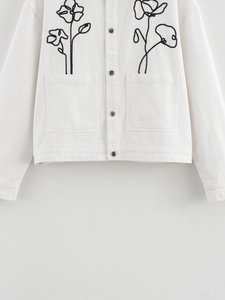 Detail of white cotton jacket featuring black floral embroidery and silver metal buttons