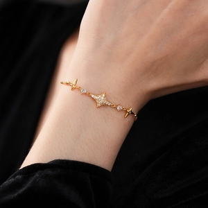 Detail of a gold starburst charm bracelet with zircons on a model's wrist