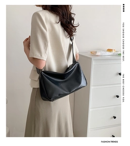 Detail of a large black soft leather tote bag worn by a model in a minimalist setting