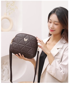 Detail of quilted dark brown crossbody bag featuring a golden butterfly metal ornament
