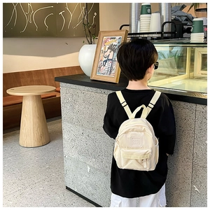 Vue arrière d'un enfant portant un sac à dos crème léger dans un intérieur élégant