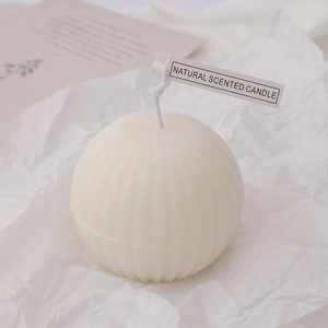 Spherical cream white scented candle with ribbed texture on white textured paper