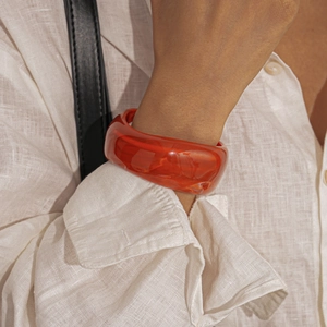 Close-up of a wide translucent red resin bangle with amber-like texture on a white sleeve