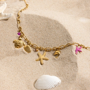 Golden ocean charm bracelet with starfish and shell pendants on a sandy beach background