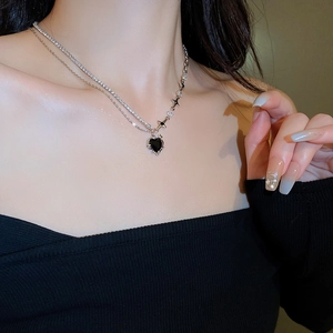 Detail of layered silver necklace with black heart pendant and star charms on model