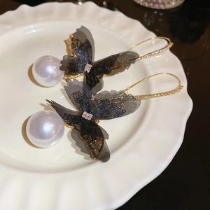 Detail of mesh butterfly earrings with large white pearls on a ceramic dish