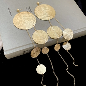Detail of long gold tassel earrings with textured round discs on a minimalist book
