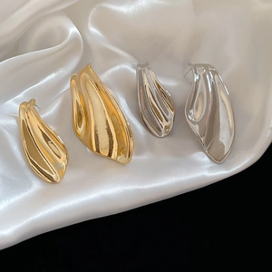 Detail view of irregular gold and silver polished fishtail earrings on white silk fabric