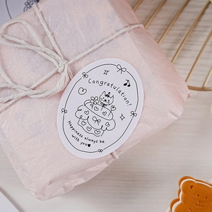 Close-up of oval Happy Birthday sticker with cat cake design on pink gift wrap