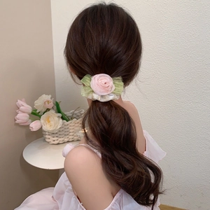 Detailed view of a pink rose hair scrunchie with green leaves on a low ponytail