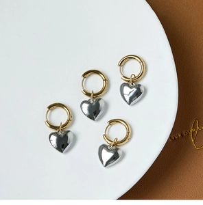 Macro detail of mixed-metal heart drop earrings on a white tray with leather background
