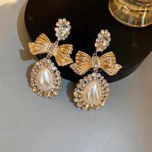 Gros plan sur les boucles d'oreilles nœud doré avec cristaux et perle goutte d'eau