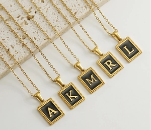 Macro detail of 18K gold stainless steel initial pendants on a beige stone surface
